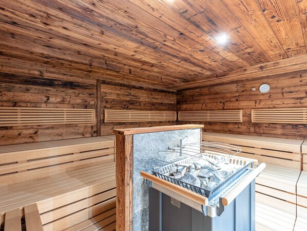 A sauna room with wooden walls and benches, a stone sauna, and a clock on the wall.