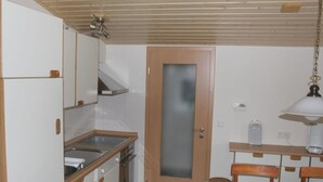 Uma cozinha compacta com forno embutido, uma pia pequena e uma mesa de jantar de madeira com cadeiras.