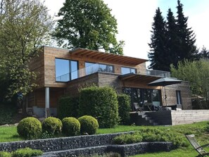 Een modern huis met twee verdiepingen, een houten gevel, grote ramen en een balkon.