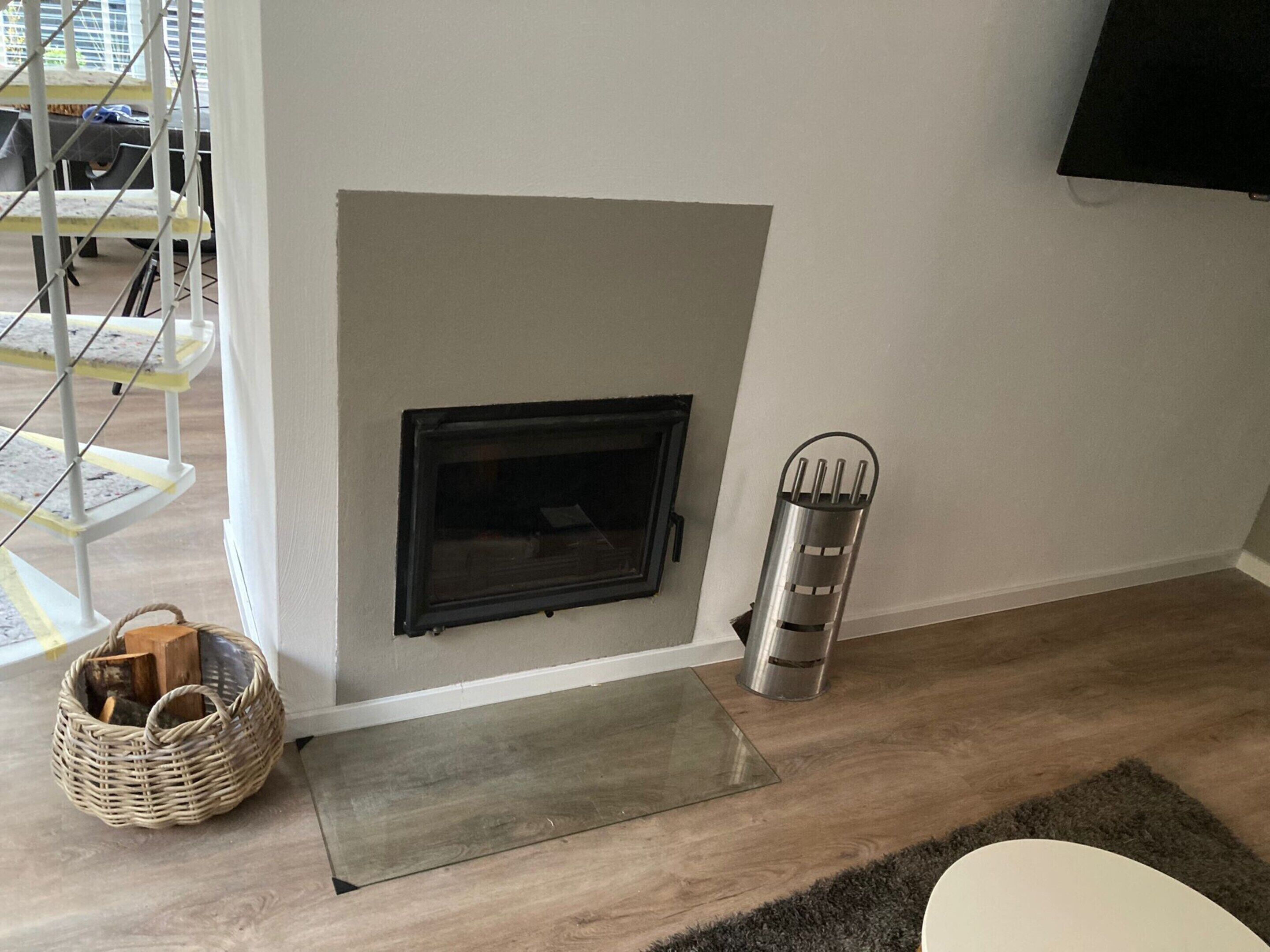 A room with a fireplace, a metal heater, a wicker basket, and a small rug.