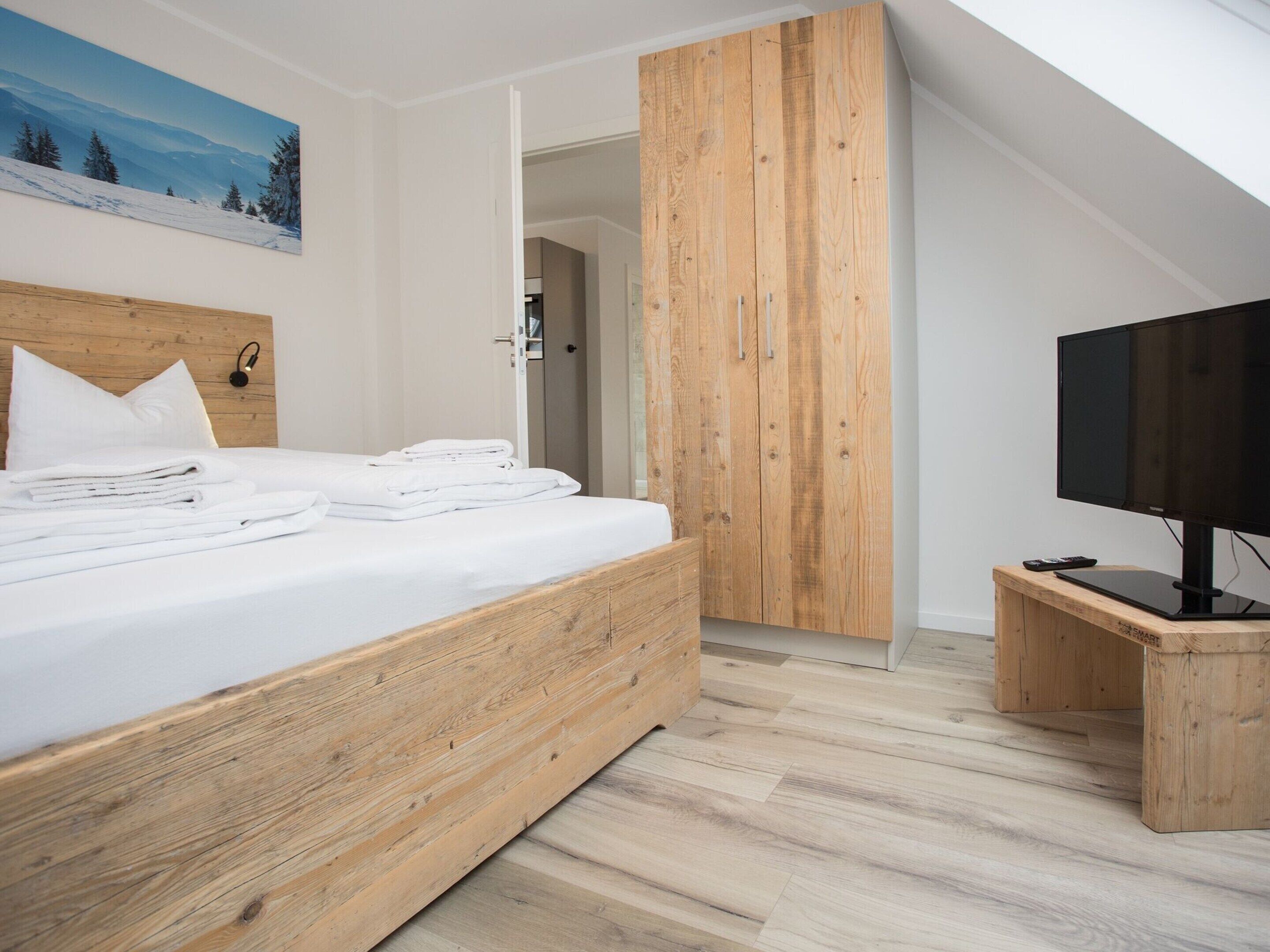 Een moderne slaapkamer met een houten bed, een televisie op een houten dressoir en een schilderij aan de wand.