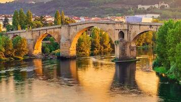 A stone bridge with multiple arches over a river, surrounded by greenery and buildings in the background.