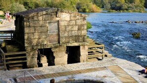 A stone building with a pool, wooden deck, and a river in the background. - Belvilla by OYO Villa Trabazos Abellas (Ourense)