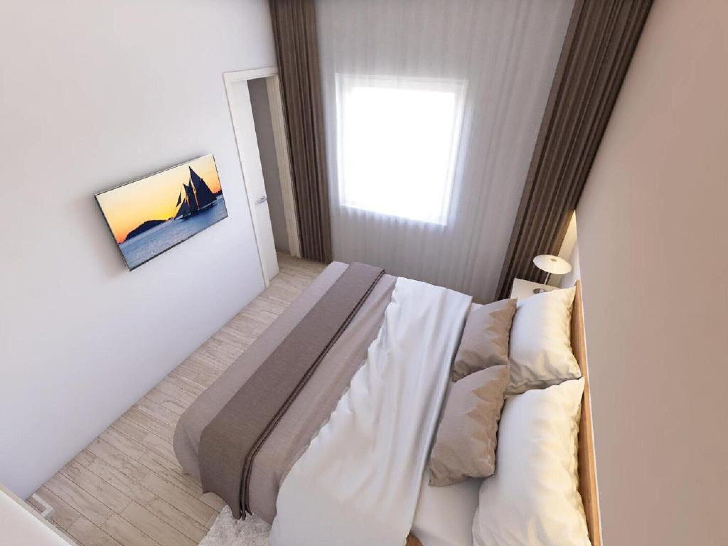 A neatly made bed with a view of a sunset through a window, a painting on the wall, and a lamp on the nightstand.