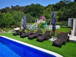 A pool area with lounge chairs, a slide, and a fenced play area.
