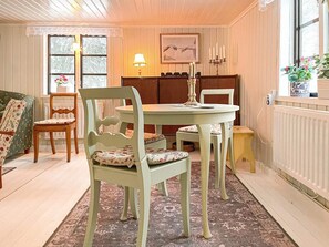 Uma área de refeições com mesa redonda, duas cadeiras, um sofá estampado com motivos florais e uma janela com vista para o verde.
