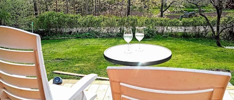 A garden patio with two white chairs and a round table with two wine glasses.