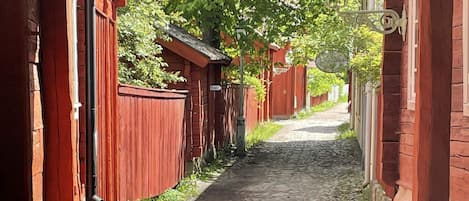 A narrow cobblestone alley flanked by red wooden buildings with a street lamp overhead.
