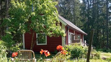 A red cabin with a porch, surrounded by lush greenery and poppies.