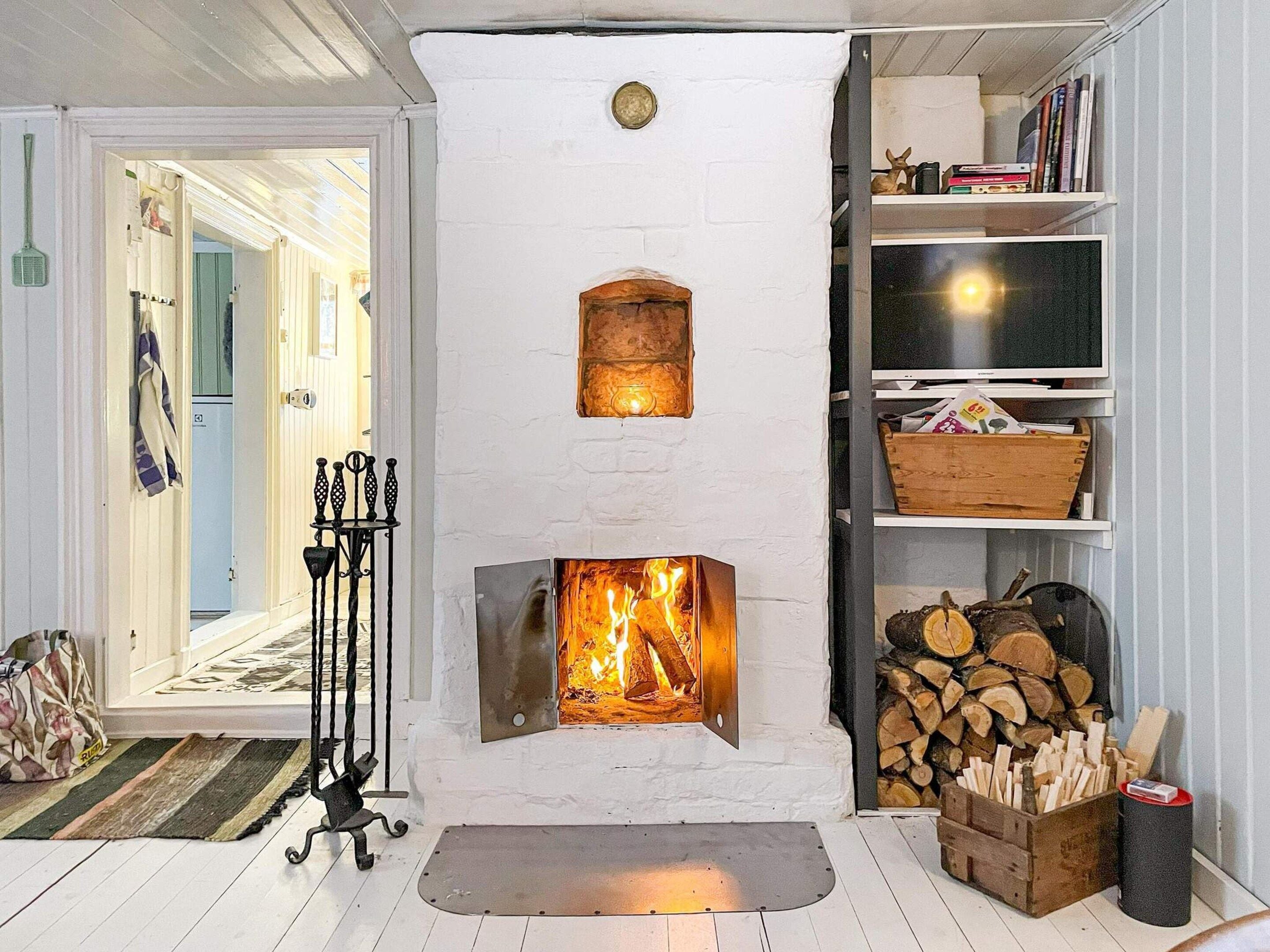 Una habitación con chimenea de ladrillo blanco, un televisor sobre una estantería y una puerta que da a otra habitación.