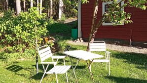 Un área de estar al aire libre con una mesa y dos sillas, rodeada de césped y árboles.