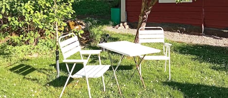 An outdoor seating area with a table and two chairs, surrounded by grass and trees.