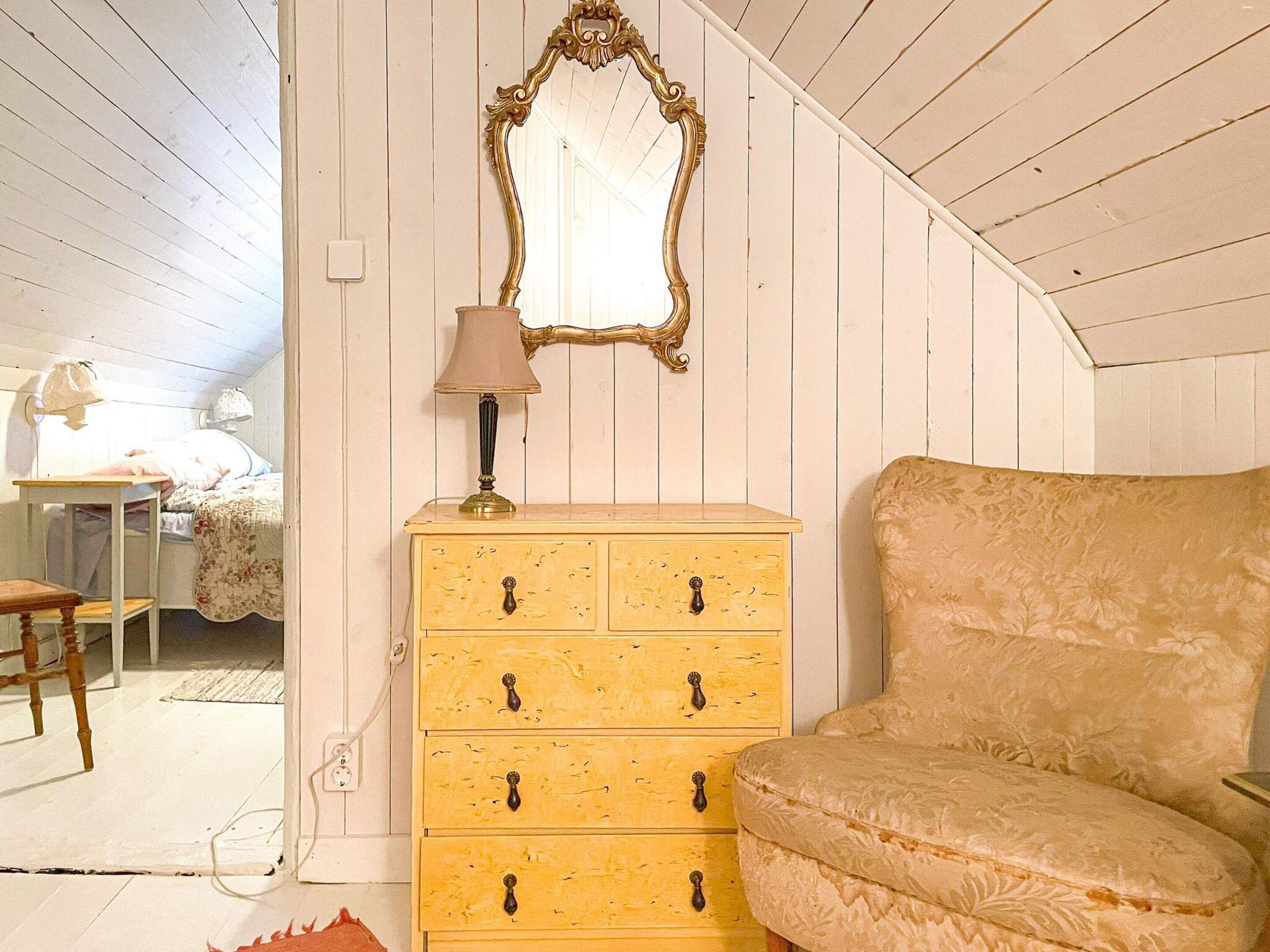 A room with a bed, a yellow dresser with drawers, a mirror, and a lamp.
