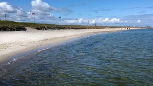 Une plage à l’eau claire, avec un rivage sablonneux et des drapeaux flottant au sommet de mâts.