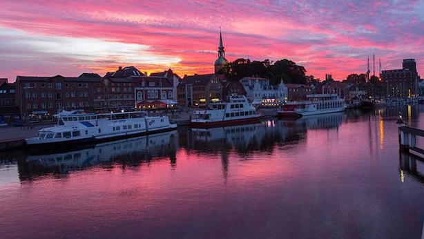 Une vue sur la ville, avec ses bâtiments historiques et ses bateaux amarrés dans le port de plaisance, au moment du coucher du soleil.
