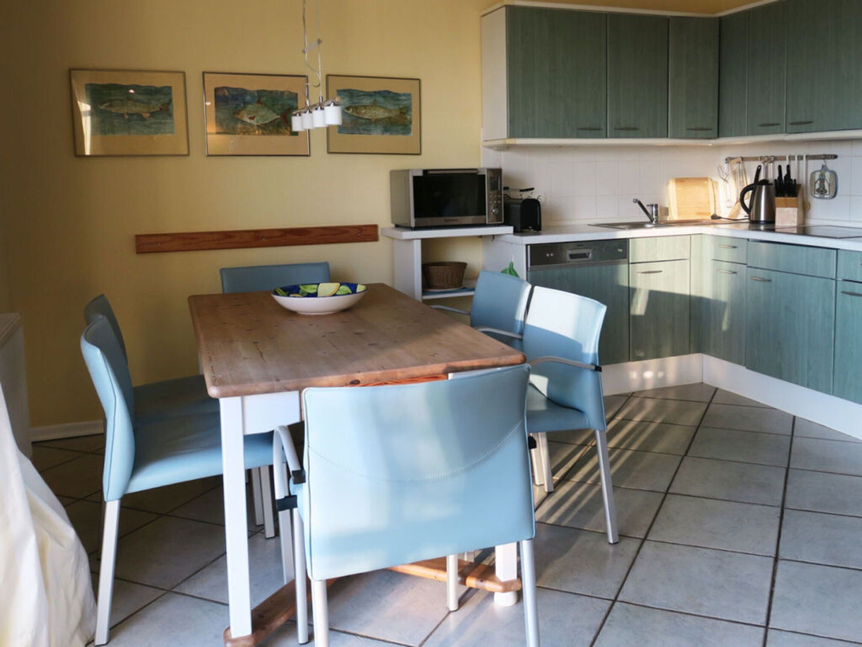 Una cocina con armarios verde azulado, una mesa de madera y sillas azules.