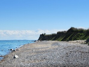 Une plage de galets, une falaise verdoyante et un ciel bleu azur.