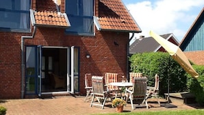Une maison en briques avec un toit en tuiles, une porte-fenêtre coulissante et une terrasse aménagée avec du mobilier d’extérieur.