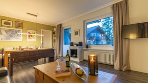 A modern living room with a wooden dining table, a fireplace, and a large window with curtains. - Hexenzauber Hahnenklee (Goslar)