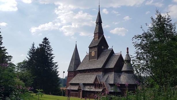 A traditional wooden building with a steeply pitched roof and multiple spires, surrounded by lush greenery. - Hexenzauber Hahnenklee (Goslar)