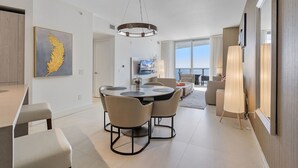 A modern living room with a dining area, a large window with a view, and a mounted TV.