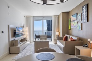 Une chambre d’hôtel moderne dotée d’un balcon, d’une télévision à écran plat, d’un canapé, d’une table à manger et d’œuvres d’art aux murs.