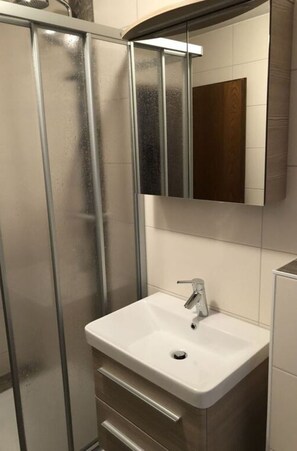 A bathroom with a glass shower enclosure, a white sink, and a mirror above it. - Holiday Home Watt Want the sea (Büsum)