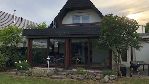 Ein modernes Haus mit einer großen Glasfront, einem Steinunterbau und einem Schornstein.