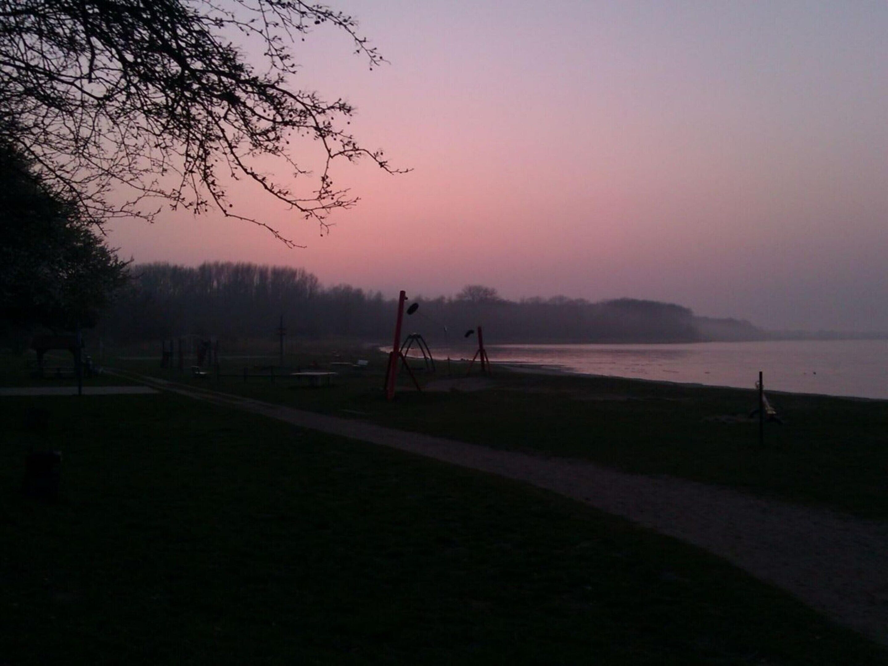 A park with a path, benches, and playground equipment near a body of water.