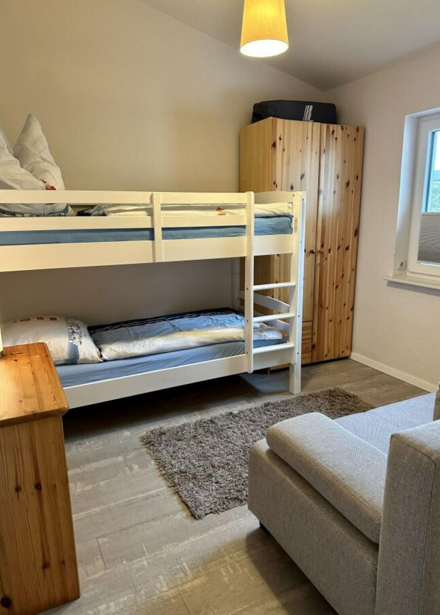 A bunk bed room with a wooden wardrobe, a grey rug, and a grey sofa.