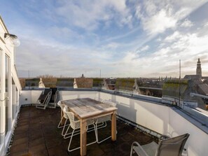A rooftop terrace with a wooden table and chairs, a view of the cityscape, and a clear sky. - Beautiful Holiday Home in Middelburg (Middelburg)