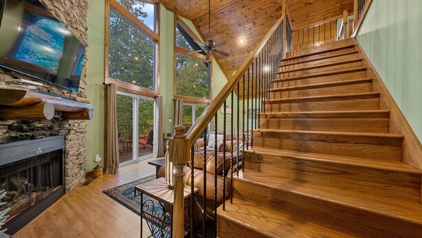 Amplia sala de estar con escalera de madera, chimenea de piedra y un gran ventanal con vistas al exterior.