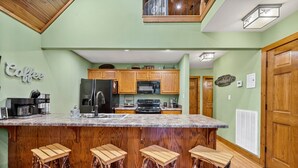 Una cocina con una isla central, taburetes de madera y un letrero que dice 'Coffee'.