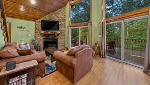 Un amplio salón con chimenea de piedra, sofás de cuero y un televisor grande.