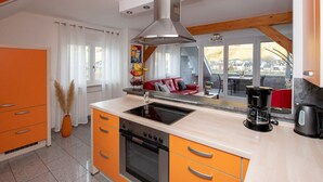 Une cuisine moderne avec des meubles de couleur orange, un four encastré et une grande fenêtre donnant sur un paysage urbain.