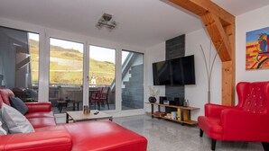 Un salon moderne avec des canapés en cuir rouge, un téléviseur à écran plat fixé au mur et un coin repas comprenant une table et des chaises.