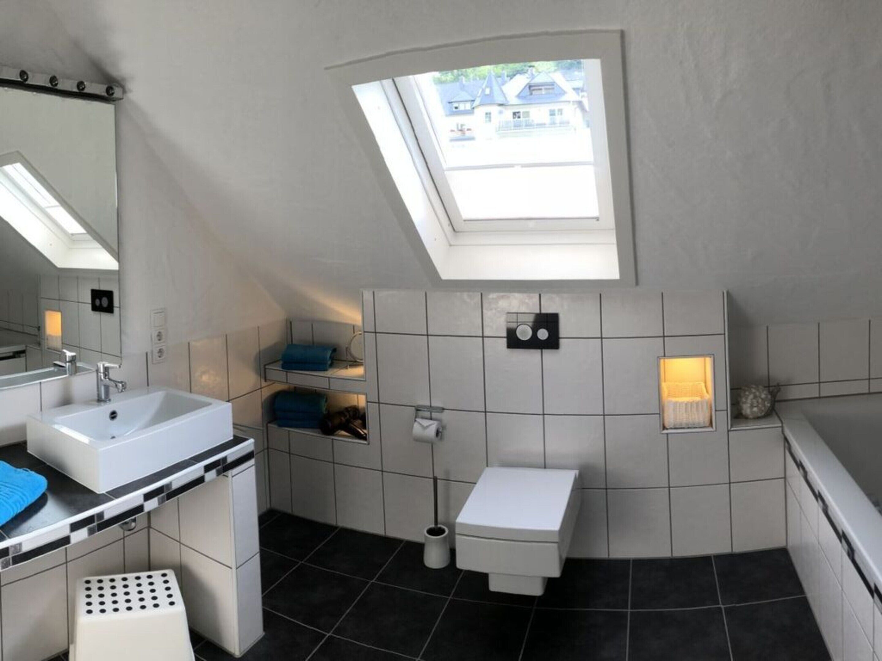 A modern bathroom with a skylight, a sink, a toilet, and a small shelf with towels.