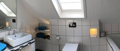 A modern bathroom with a skylight, a sink, a toilet, and a small shelf with towels.