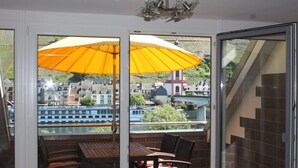Un balcon avec une table et des chaises, de grands parasols jaunes et une vue sur une ville et une rivière.