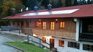 Un edificio de madera de dos pisos con techo de tejas rojas, un balcón de madera y un camino de piedra que conduce a la entrada.