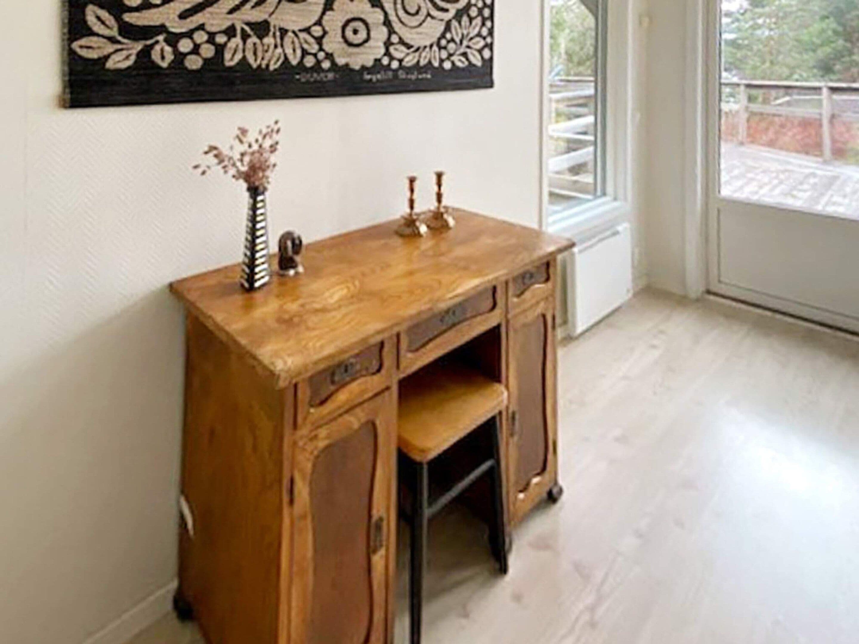 Un mueble de madera con cajones y estantes, un jarrón con flores, y un adorno de pared.