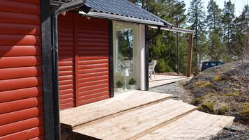 A wooden deck leading to a glass door entrance of a building with a red exterior and a metal roof.