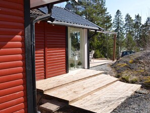 A wooden deck leading to a glass door entrance of a building with a red exterior and a metal roof.