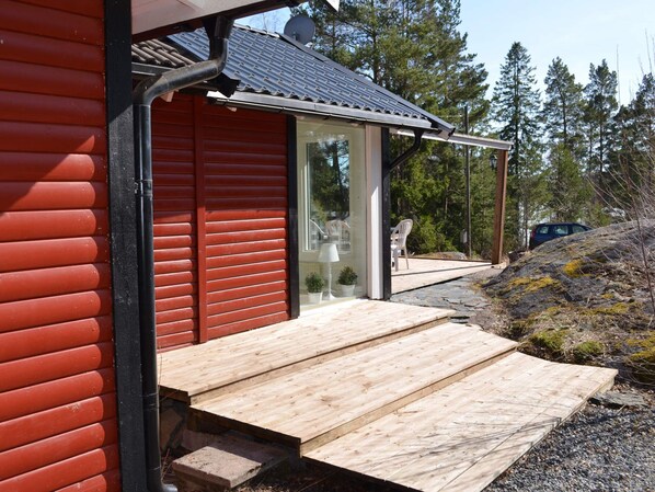A wooden deck leading to a glass door entrance of a building with a red exterior and a metal roof.