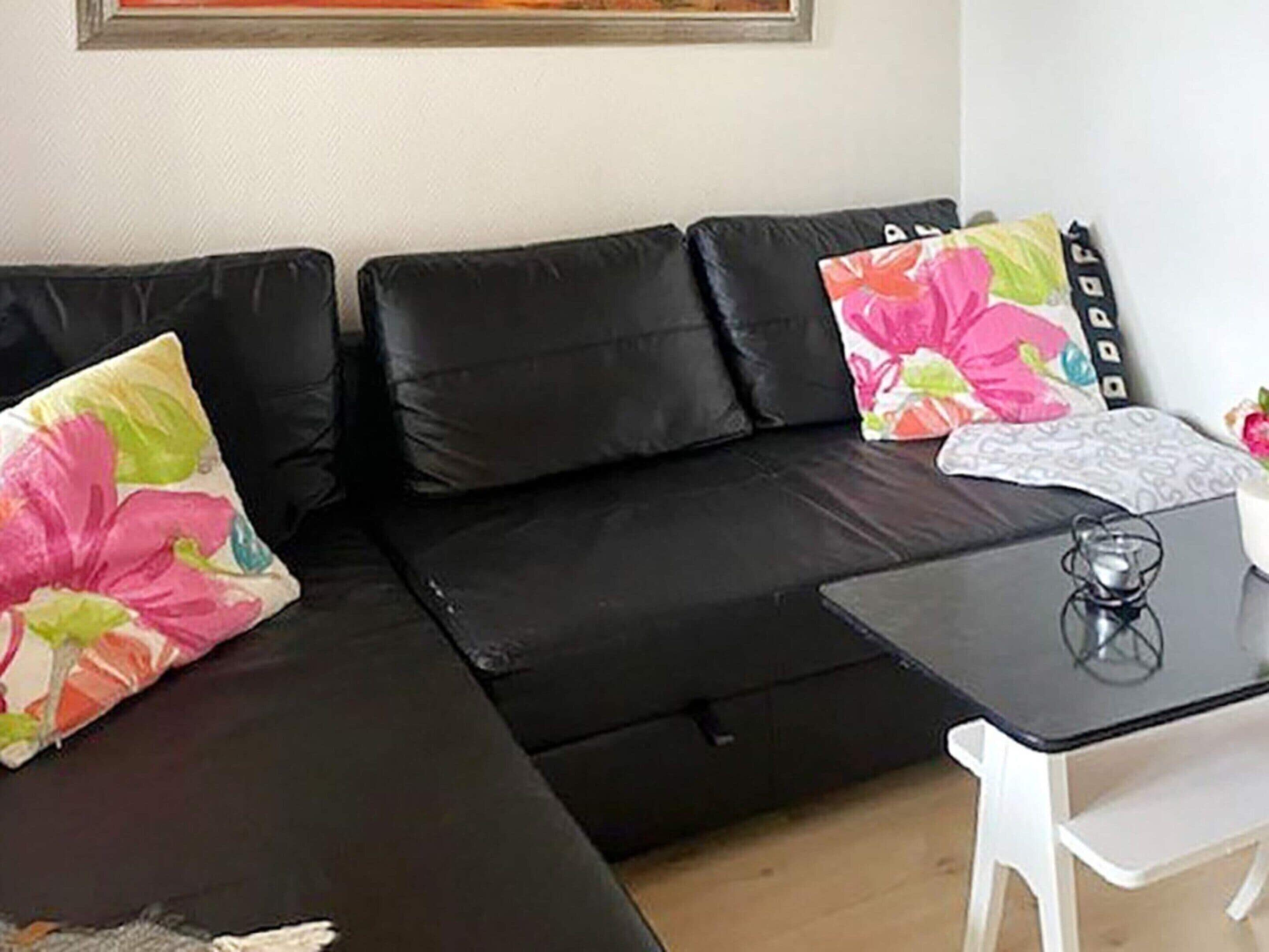 Ein schwarzes Ledersofa mit floralen Kissen, ein kleiner Tisch mit einem Glasobjekt und ein weißer Sessel.
