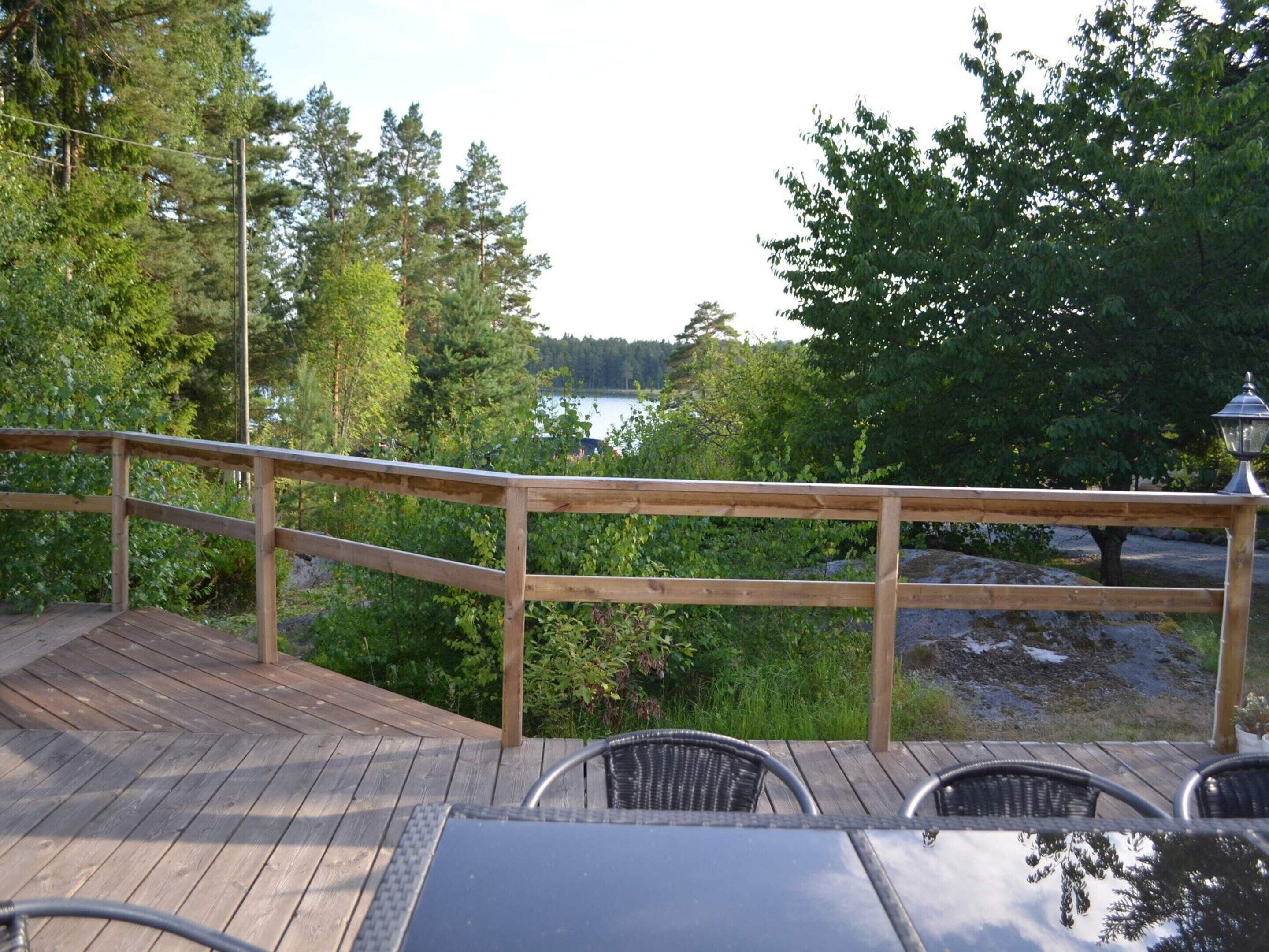 Une terrasse en bois avec une rambarde donnant sur un lac, entourée d’arbres.
