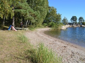 A sandy beach with a clear lake, surrounded by trees and a playground.