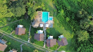 Vue aérienne d’un complexe hôtelier comprenant plusieurs hébergements de type bungalow, une piscine centrale et une végétation luxuriante environnante.