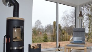 Un salon moderne doté d’un poêle à bois, d’un fauteuil confortable et d’une grande fenêtre donnant sur l’extérieur.