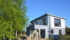 Une maison moderne à deux étages, dotée d’un balcon, entourée d’arbres et d’une pelouse.